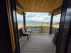 A wooden deck with chairs, a view of houses and mountains, and a cloudy sky.