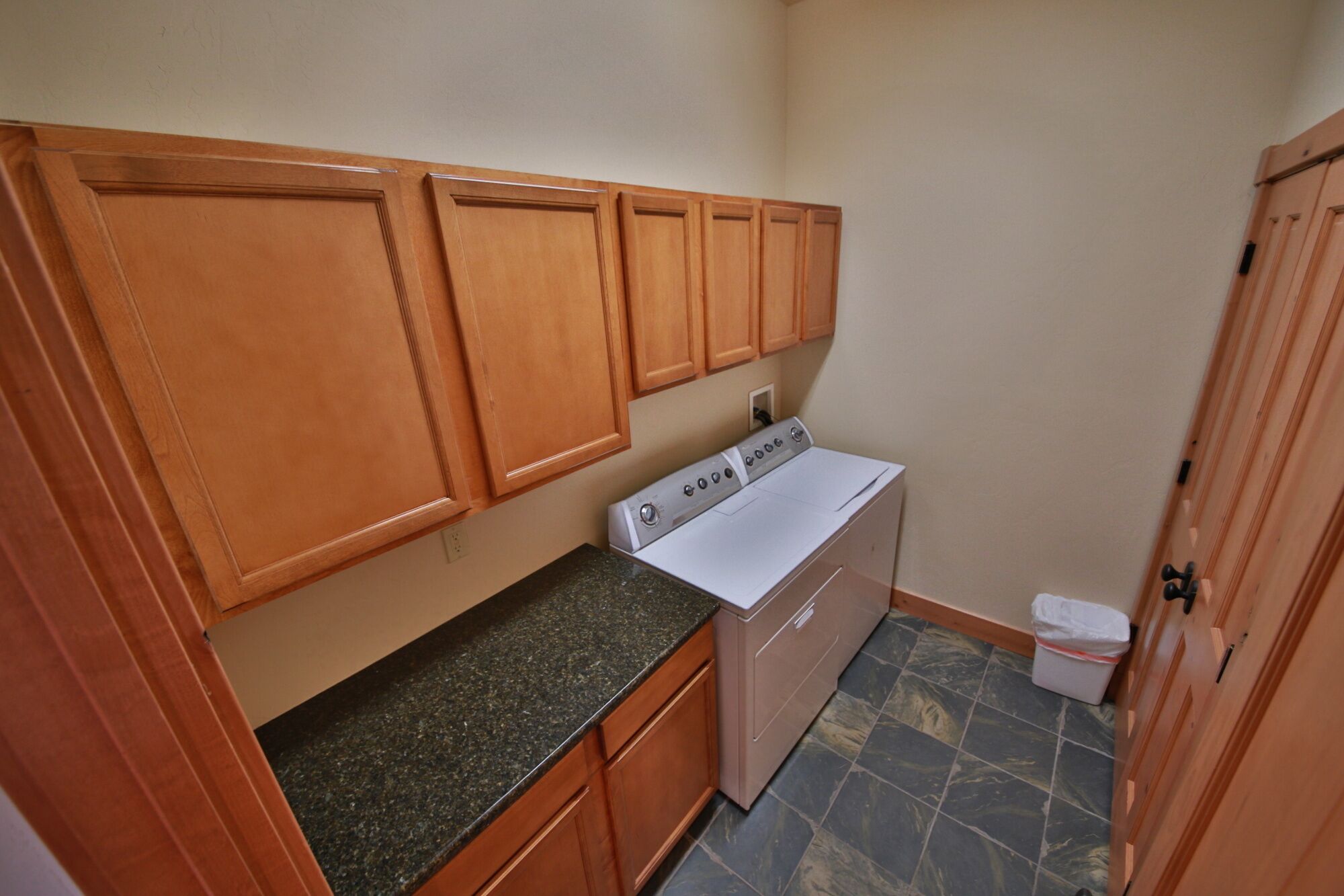 A compact kitchen with wooden cabinets, a granite countertop, a built-in washer and dryer, and a tiled floor.
