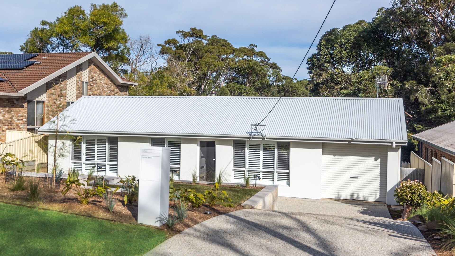 A single-story house with a flat roof, a front garage, and a well-maintained front yard with small plants and a lawn.