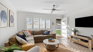 A modern living room with a leather sofa, a round coffee table, and a flat-screen TV mounted on the wall. - The Haven in Mollymook (Mollymook Beach)