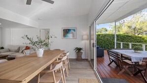 A spacious indoor area with a wooden dining table and chairs, a sofa, and a potted plant. - The Haven in Mollymook (Mollymook Beach)