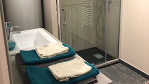 Un baño moderno con cabina de ducha de vidrio, una bañera blanca y toallas ordenadas sobre una encimera.