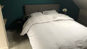 Un dormitorio con cama, mesita de noche, un jarrón con flores y una pared de acento color turquesa.