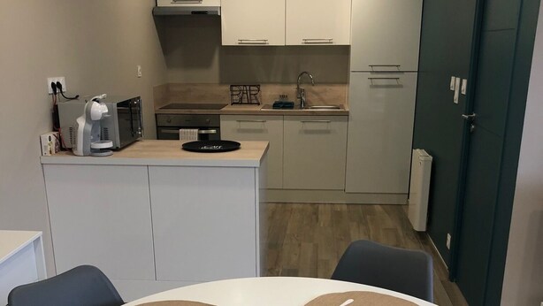 Una cocina moderna con armarios blancos, una cafetera y un comedor con una mesa redonda y posavasos.