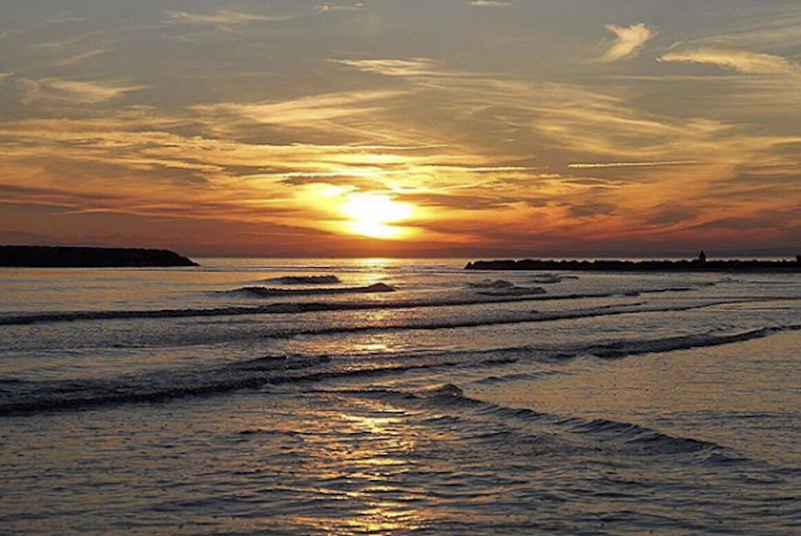 Un coucher de soleil sur une plage, avec des vagues et une côte lointaine.