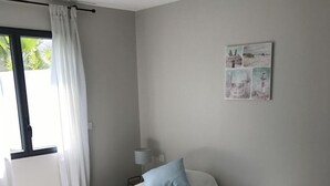 Ein Zimmer mit zwei Einzelbetten, einem Fenster mit weißen Vorhängen, einer Wandlampe und einem kleinen Gemälde.