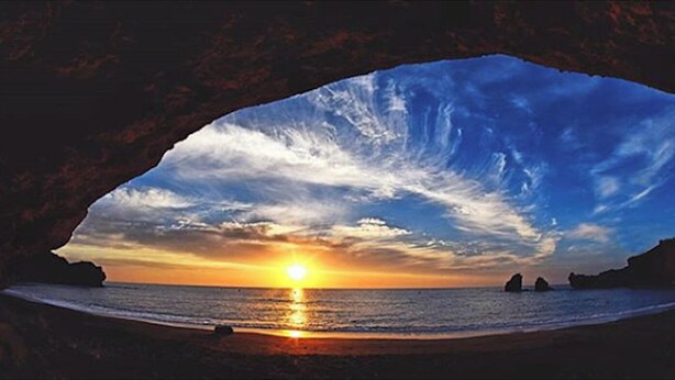 Ein Sonnenuntergang über einem Strand, wobei eine hohlen Struktur die Aussicht einfasst.