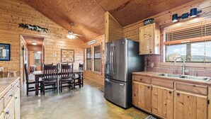 Interior de una cabaña de madera con comedor, cocina y un ventanal con vistas.