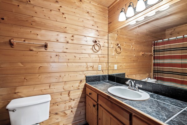 A wooden cabin bathroom with a toilet, sink, and mirror.