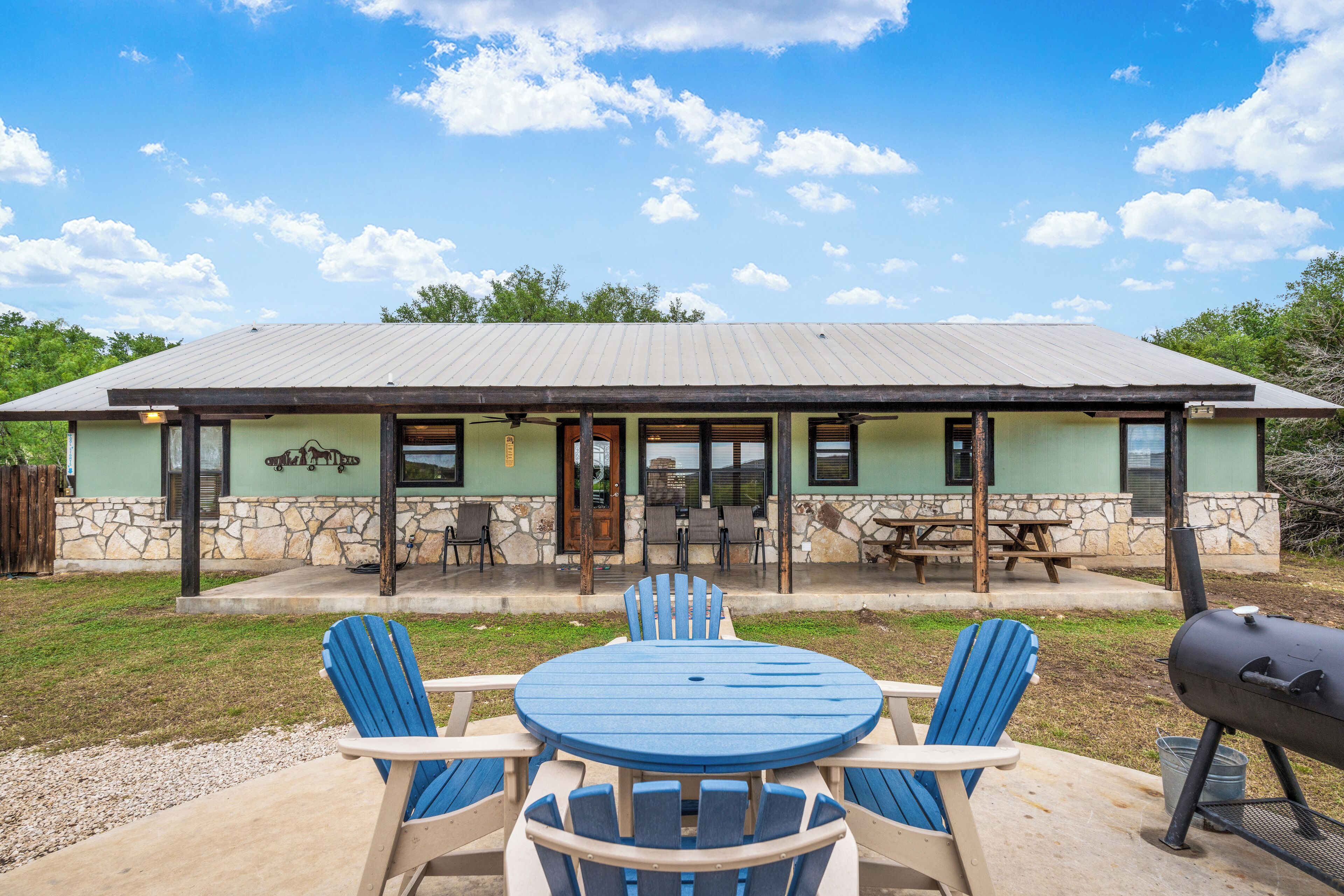 A house with a patio, a barbecue grill, and a table with chairs.