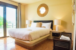 A hotel room with a large bed, two bedside lamps, a round mirror, and a small table with a decorative item.