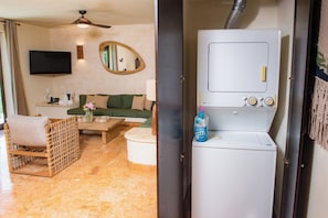 A room with a sofa, a wicker chair, a coffee table, a television, and a washing machine.