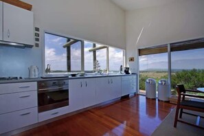 A modern kitchen with large windows, a dining area with a view, and a clean, minimalist design. - Dunes Retreat - amazing views of the ocean beach (St Andrews Beach)