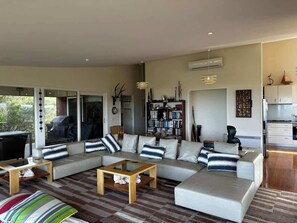 A modern living room with a sectional sofa, a coffee table, and a bookshelf. - Dunes Retreat - amazing views of the ocean beach (St Andrews Beach)