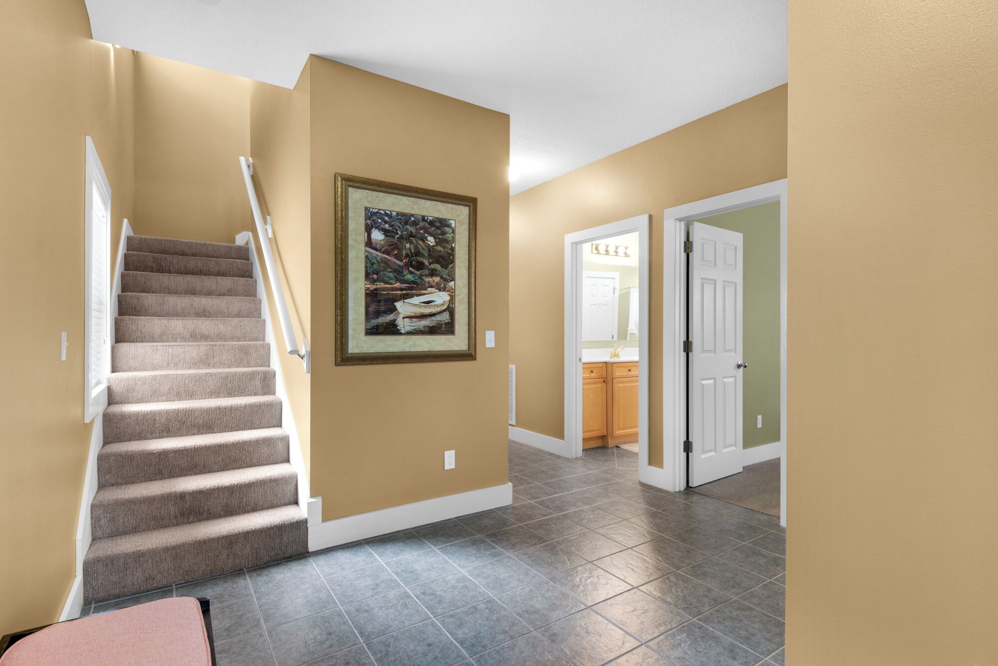 A hallway with beige walls, a carpeted staircase, a framed painting, and a door leading to a bathroom.