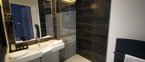 A modern bathroom with a glass-enclosed shower, a large mirror, and a white sink with a towel.