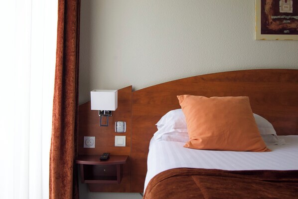 A hotel room with a wooden headboard, a single bed with white and orange bedding, a bedside table with a lamp, and a wall-mounted phone. - Hôtel Golf St Lazare (Limoges)