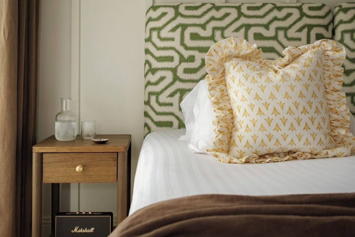 A hotel room with a bed, a nightstand with a lamp, a radio, and a patterned headboard.