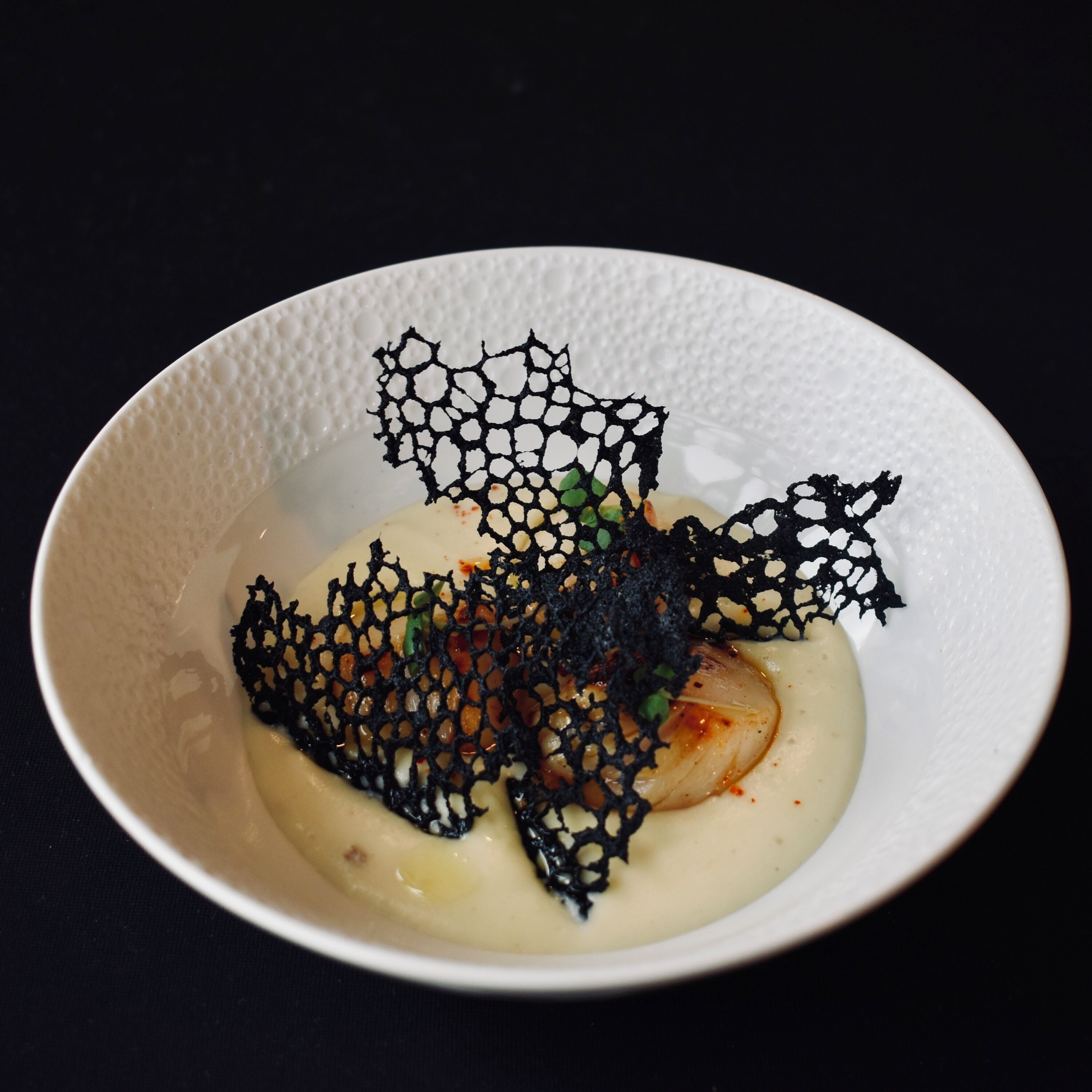 A white bowl with a dessert featuring a net-like structure and a creamy base.