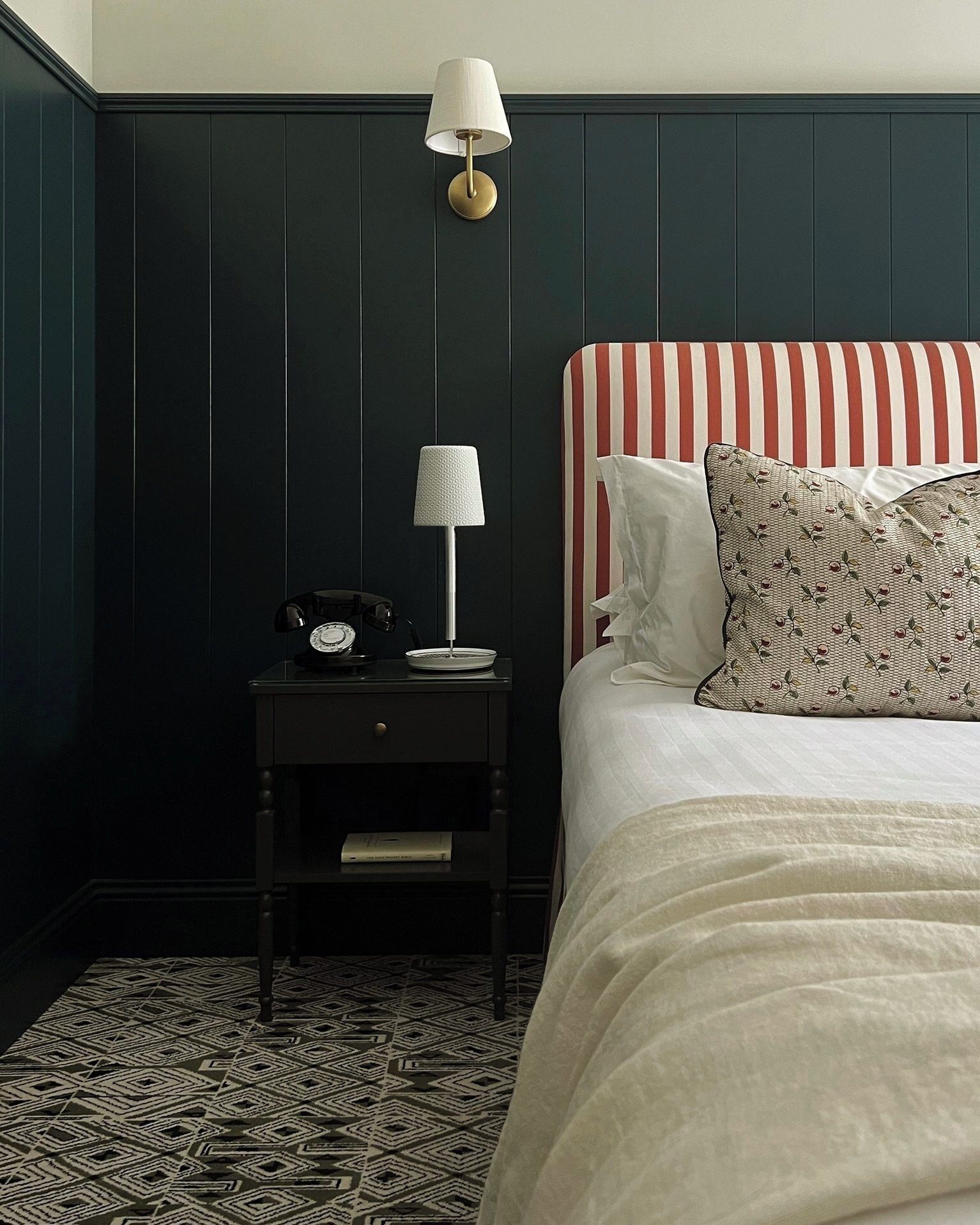 Une chambre à coucher avec un lit, une table de chevet avec une lampe, une horloge et un tapis à motifs.