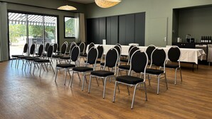 Un salón de conferencias con filas de sillas, una larga mesa e iluminación colgante.
