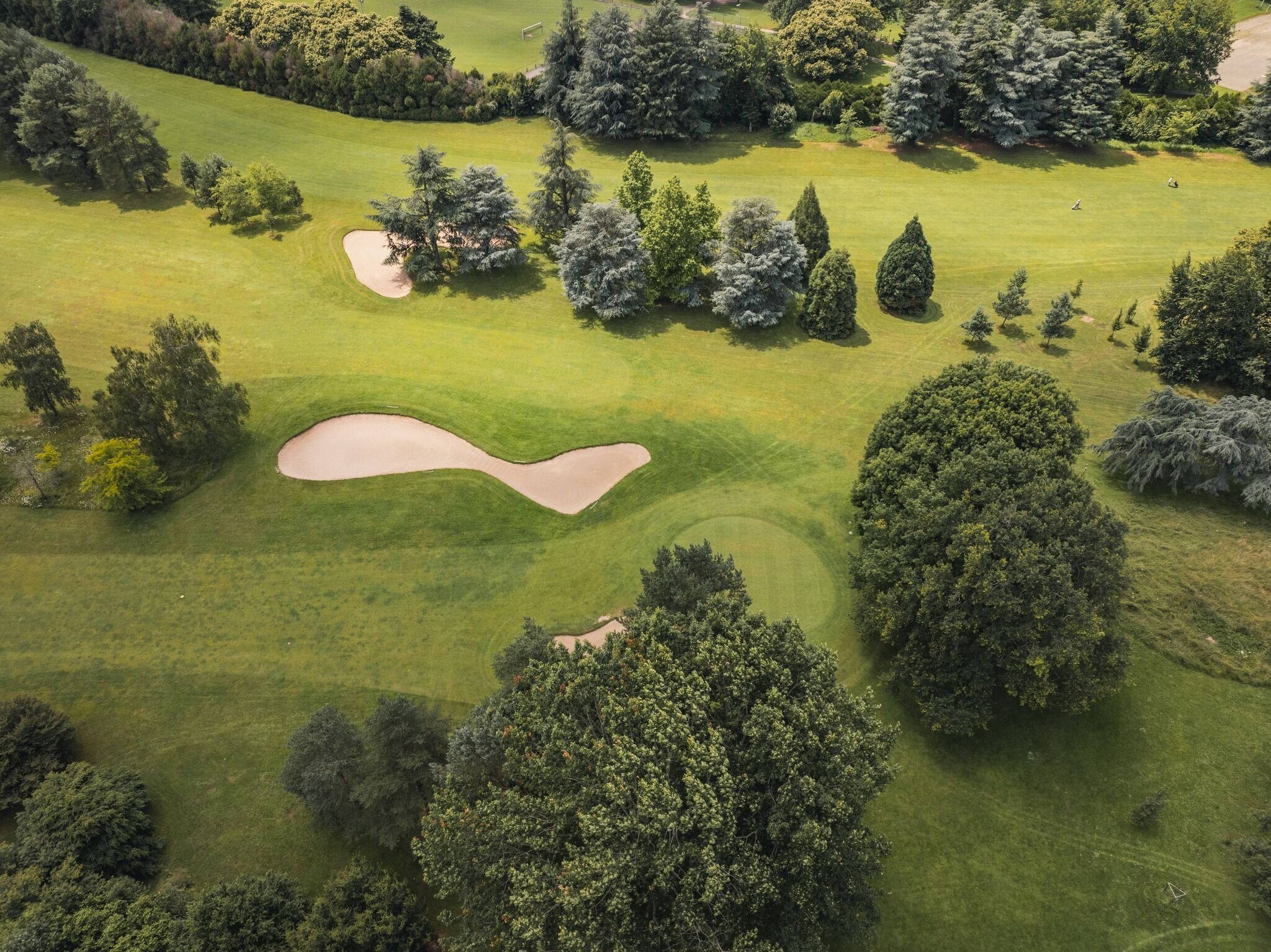 Vue aérienne d’un parcours de golf avec des bunkers de sable, des arbres et un terrain verdoyant bien entretenu.