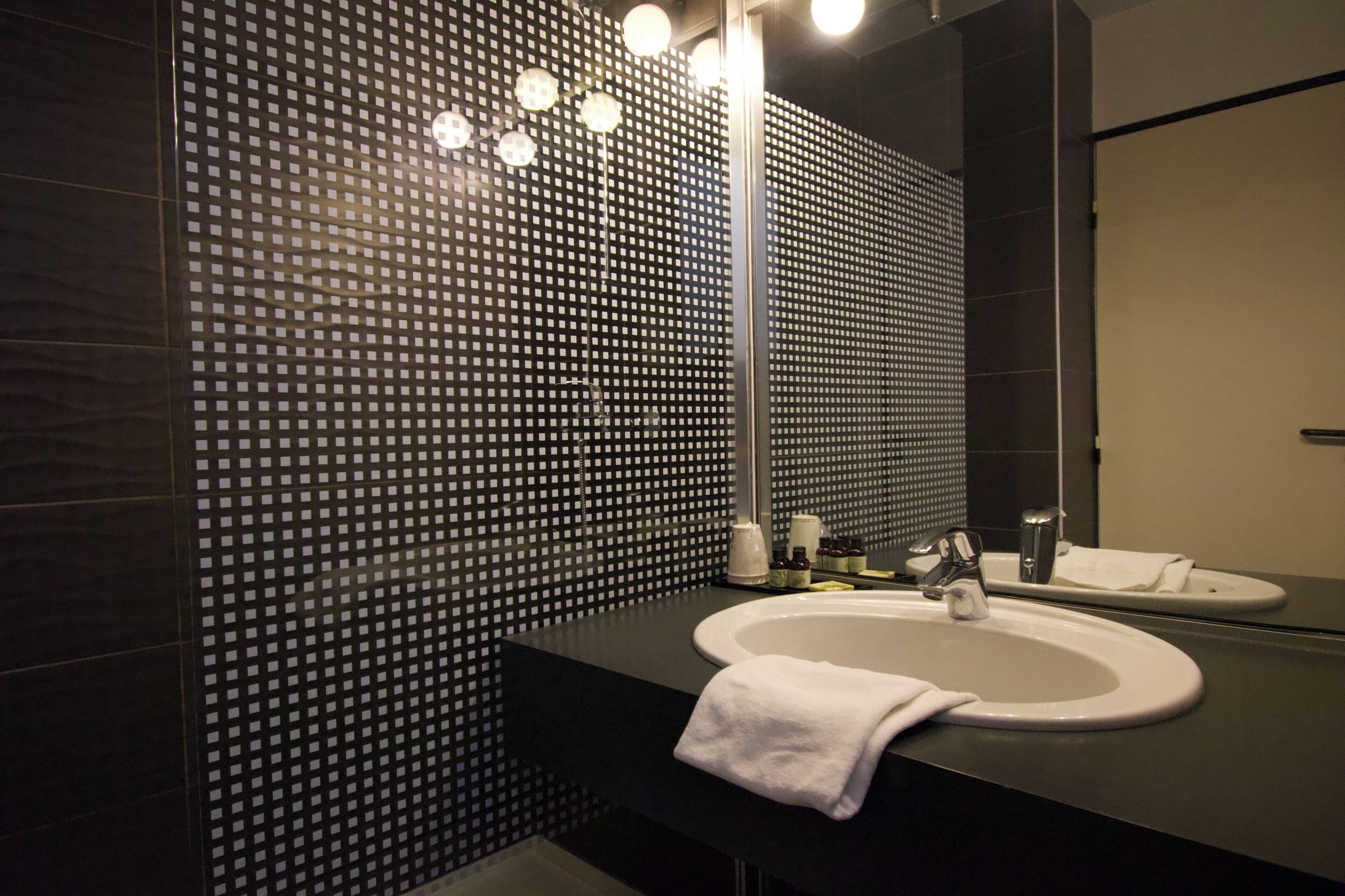 Un bagno moderno con una parete rivestita in piastrelle nere, un lavabo rotondo e uno specchio.