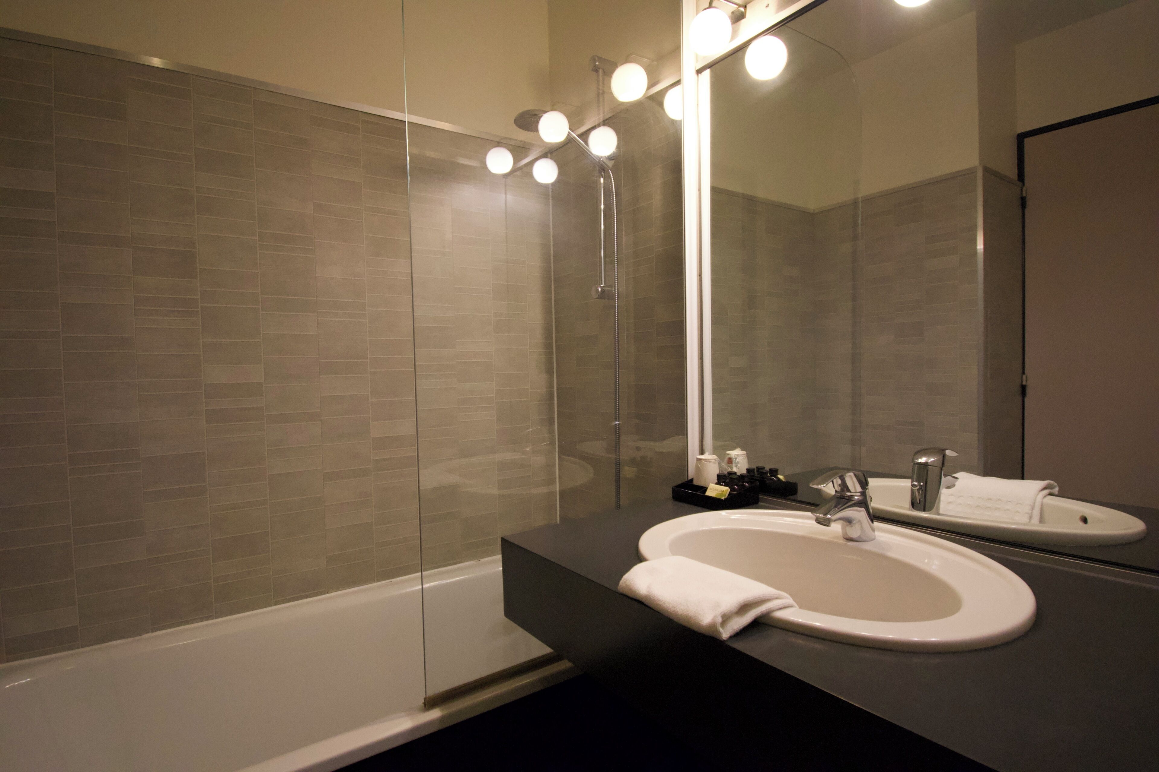 Un baño moderno con ducha de vidrio, encimera negra, lavabo blanco y un espejo grande con luces.