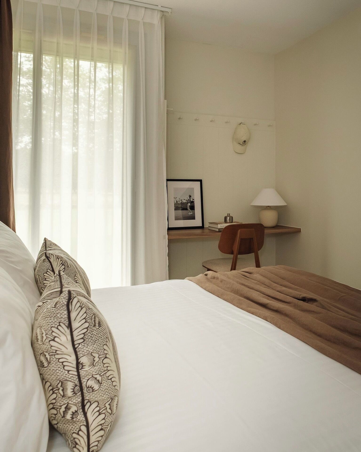 Ein Schlafzimmer mit einem Bett, einem Nachttisch aus Holz, einem Schreibtisch mit Stuhl, einer Lampe und einem gerahmten Bild an der Wand.