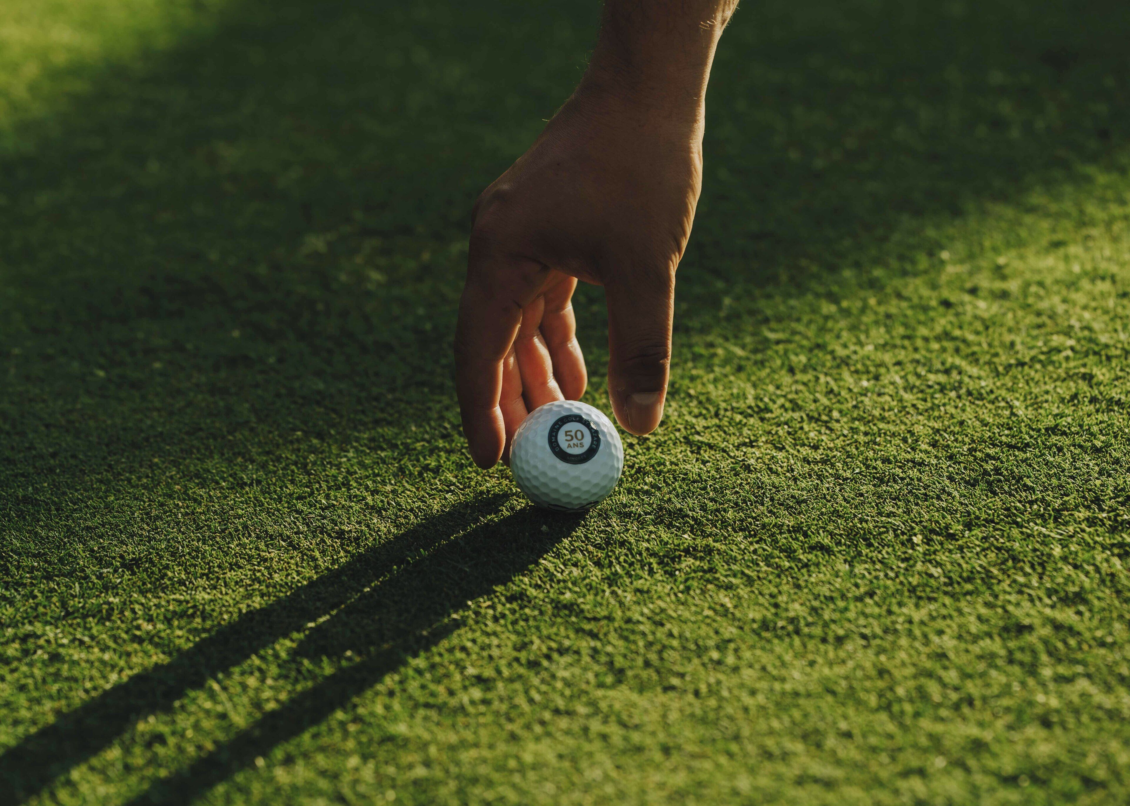A hand placing a golf ball on a green surface.