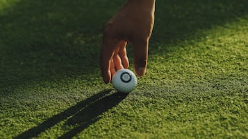 A hand placing a golf ball on a green surface.