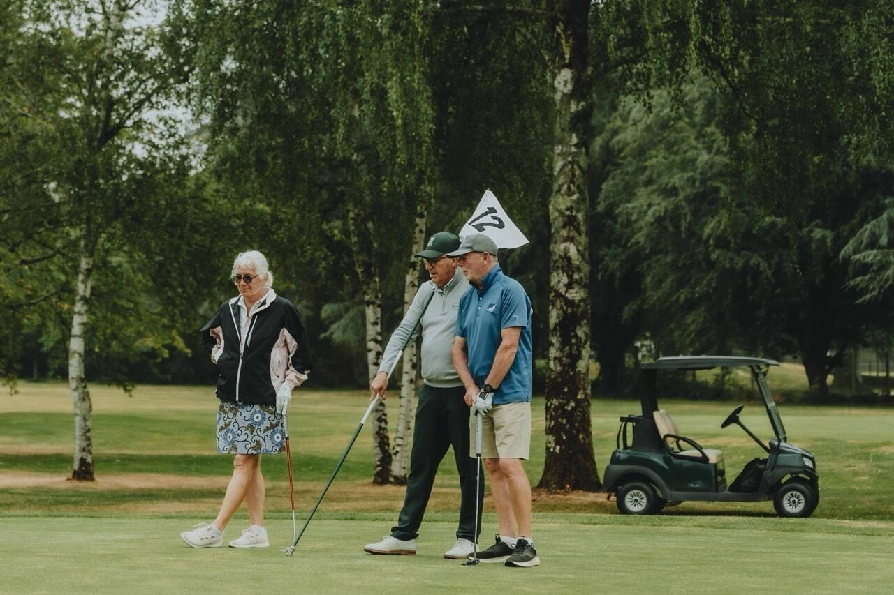 Three people on a golf course with a golf cart.