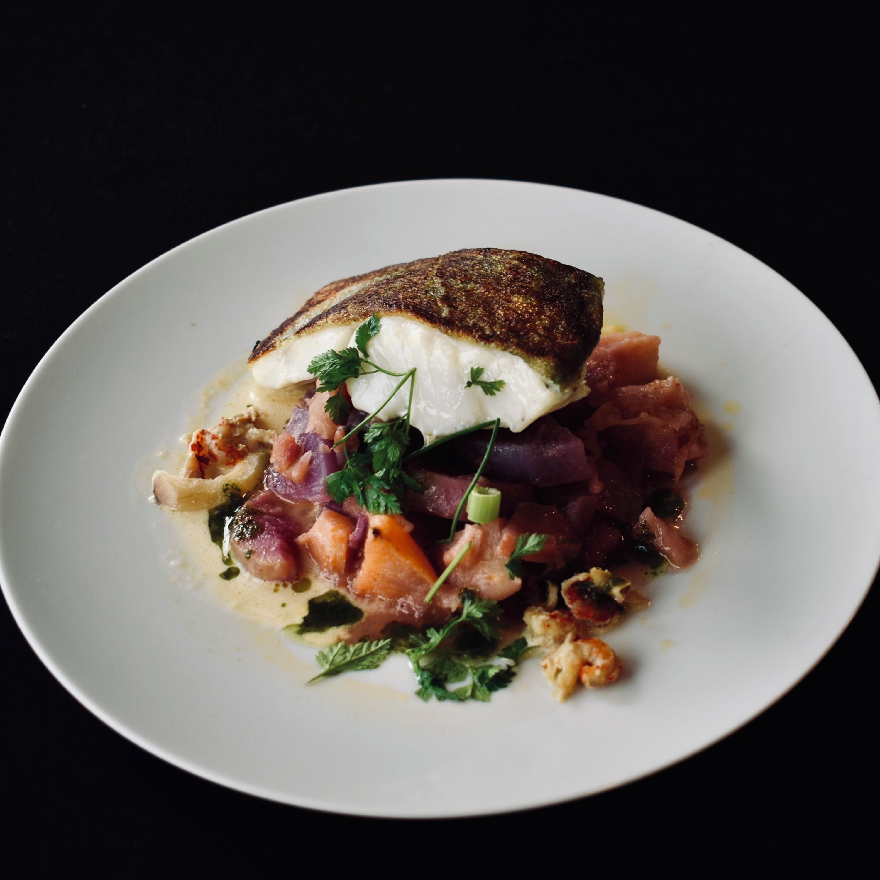 Un plato blanco con un trozo de pescado, verduras cortadas en cubos y hierbas.
