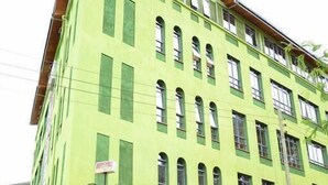 A multi-story building with a green facade, multiple windows, and a central entrance with a door. - Greenvale Hotel (Ruiru)