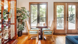 Une pièce comprenant une table en bois, deux chaises à rayures, une grande plante en pot et une vitrine contenant divers objets.