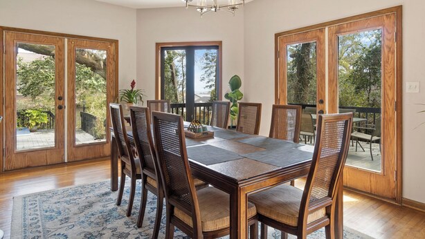 Une salle à manger avec une grande table et des chaises en bois, de grandes fenêtres et un lustre.