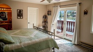 Ein Schlafzimmer mit Bett, Deckenventilator, Fenster mit Vorhängen, einer Tür und Blick auf einen Balkon mit Geländer.
