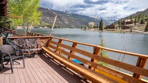 Eine Holzterrasse mit Gartenmöbeln mit Blick auf einen See und Berge.