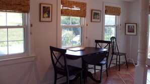 A dining area with a round table and four chairs, two windows with blinds, and framed pictures on the walls. - Luxury Country Cottage with Spectacular Blue Ridge Mountain Views! (Stanardsville)