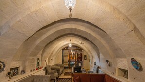 A cozy interior with a vaulted ceiling, a sofa, a chair, and a table with a remote control. - Lucky Cave Cappadocia (Nevsehir)