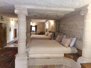 Une chambre avec deux lits, une armoire en bois, un tapis à motifs et un mur en pierre orné de sculptures.