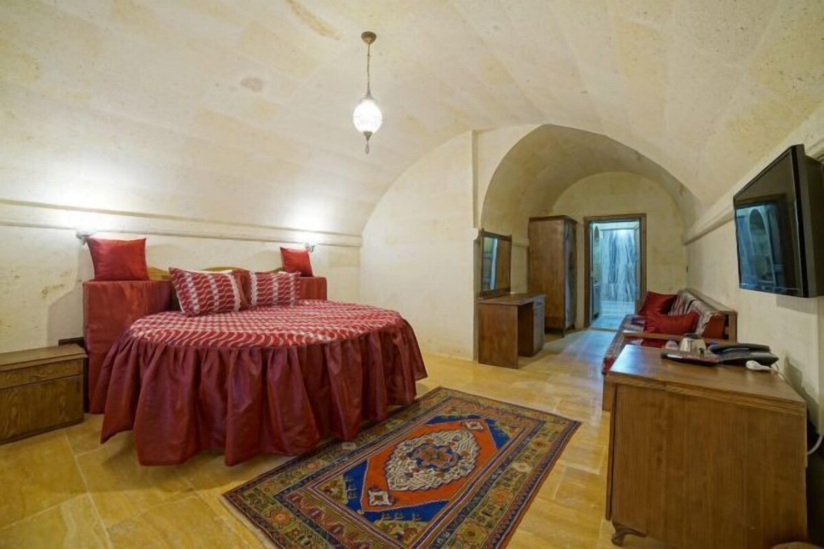 A bedroom with a bed, a desk, and a chair. There is a rug on the floor and a ceiling light.