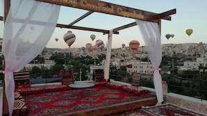 A cozy outdoor seating area with a view of Cappadocia's rock formations and hot air balloons. - Lucky Cave Cappadocia (Nevsehir)