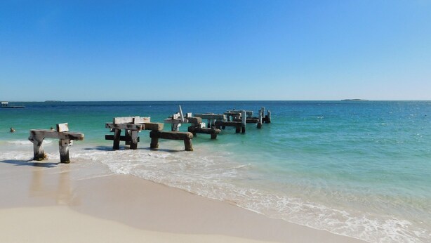 A beach with wooden structures extending into the water, a clear sky, and calm sea.