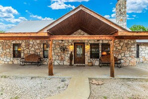 Rustic stone building with a gabled roof and stone chimney, featuring a wooden porch and metal gate.