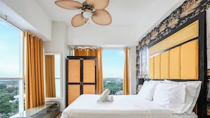 Hotelkamer met een groot bed, een plafondventilator, uitzicht op de stad en een balkon met gordijnen.