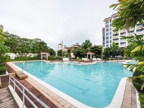A swimming pool with lounge chairs and a gazebo, surrounded by greenery and a multi-story building. - Mactan Condo. Free breakfast ! Large 1 bedrm Condo, Ocean views, Beach Access. (Lapu-Lapu City)