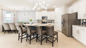 A modern kitchen with white cabinets, a central island with bar stools, stainless steel appliances, and pendant lighting. - Colorful Bright Home with Fun Loft in Encore (Kissimmee)