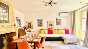 Una habitación con una mesa de comedor preparada para cuatro personas, un sofá con cojines de colores, una chimenea y obras de arte enmarcadas en las paredes.