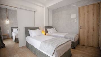 A modern bedroom with two single beds, a wooden wardrobe, and a small bedside table.